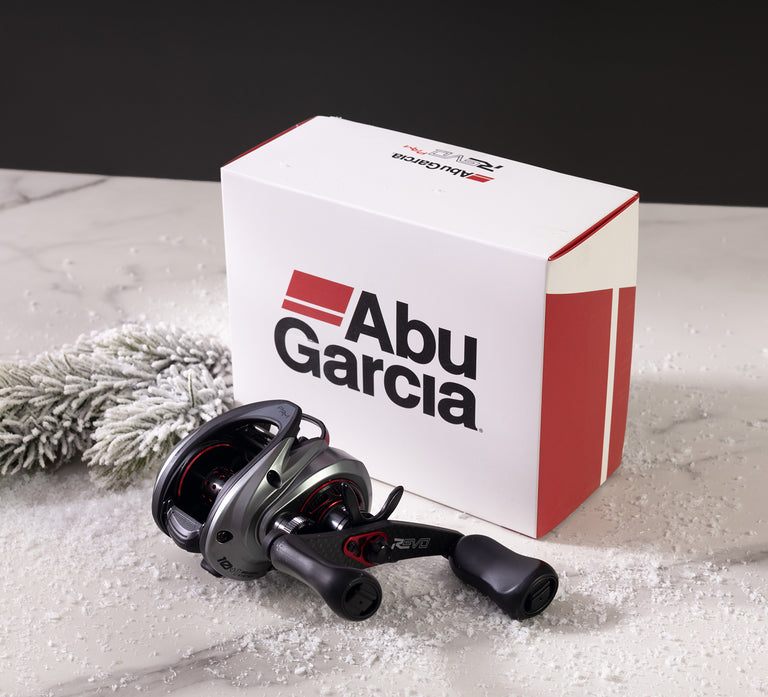 Abu Garcia Revo Low Profile Baitcast Reel on a snowy background with a box with Abu Garcia branding in the background. 