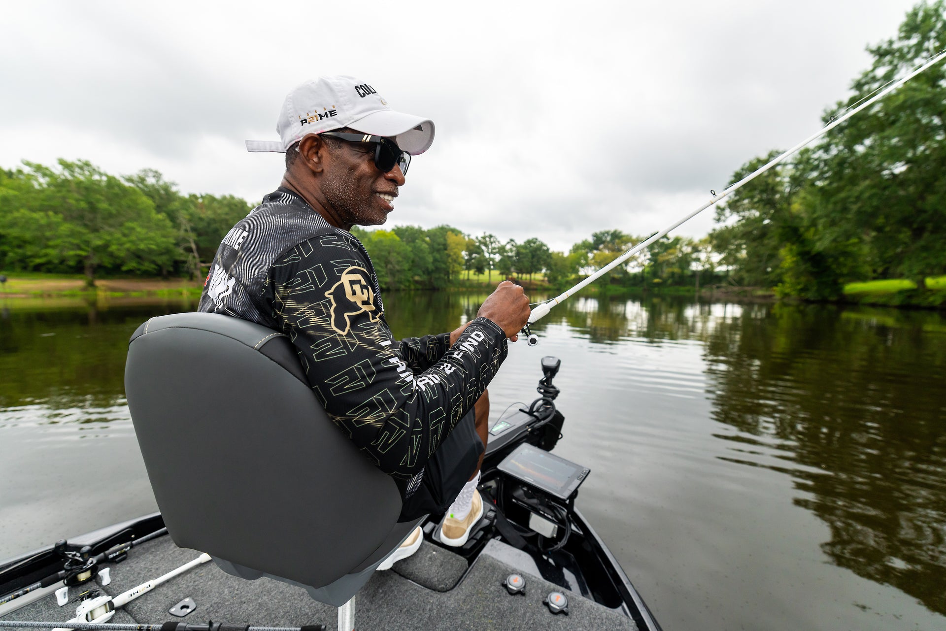 Coach Prime fishing from a boat on a calm lake with trees in the background