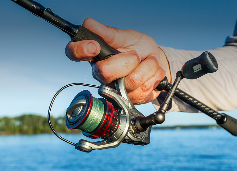 Hand holding a fishing reel with a blurred background of water and sky