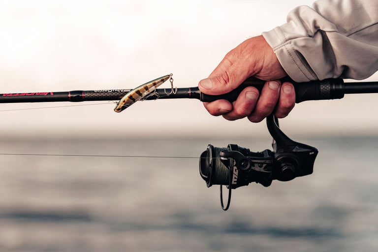 Hand holding n Abu Garcia Max Combo with a worm on a blurred water background