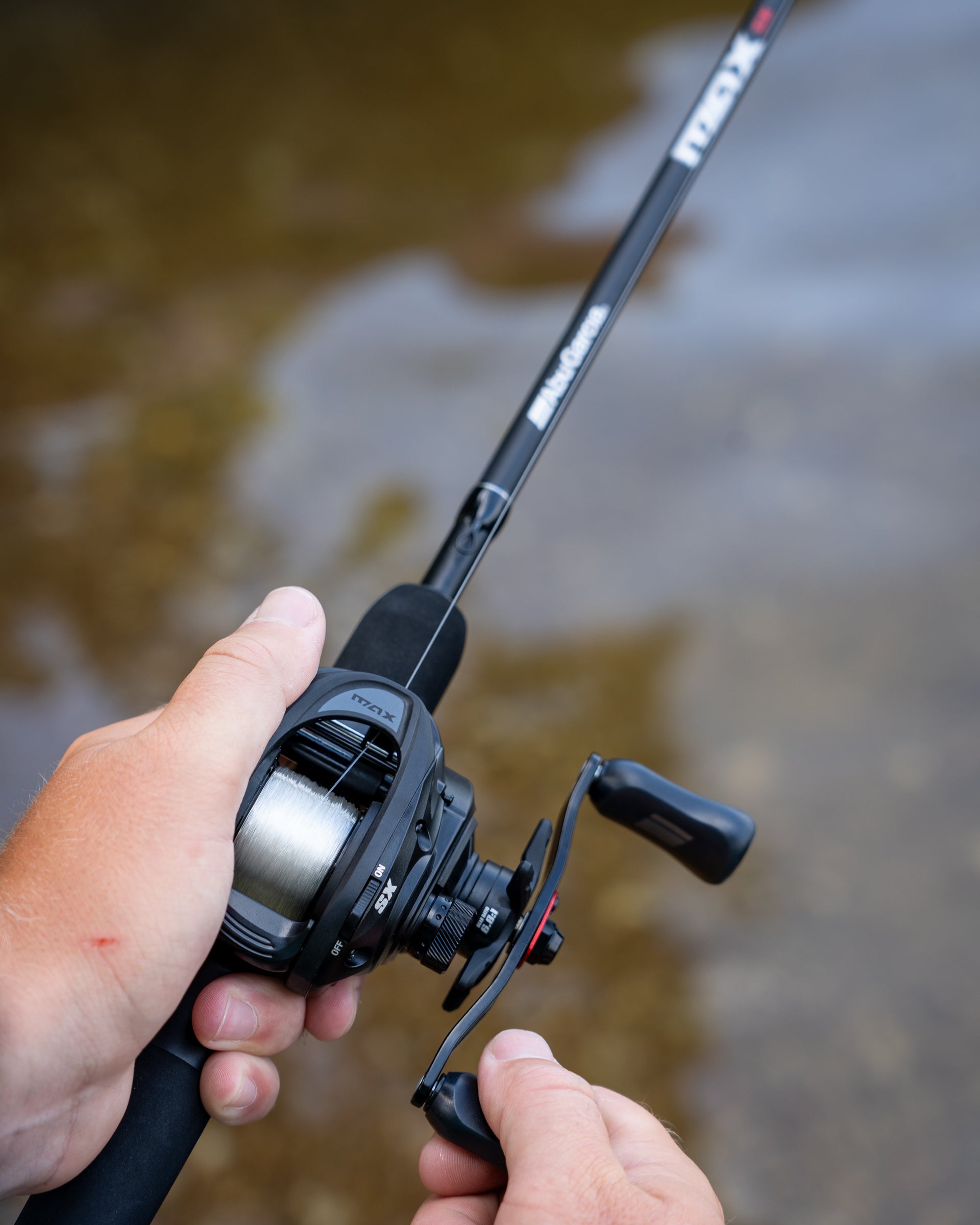 Max™ SX Flipping Switch Low Profile Reel in hand over blurred water
