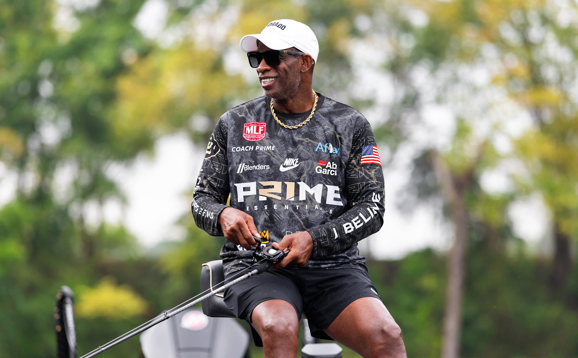 Person wearing a camouflage shirt with various logos and text, standing outdoors with trees in the background.
