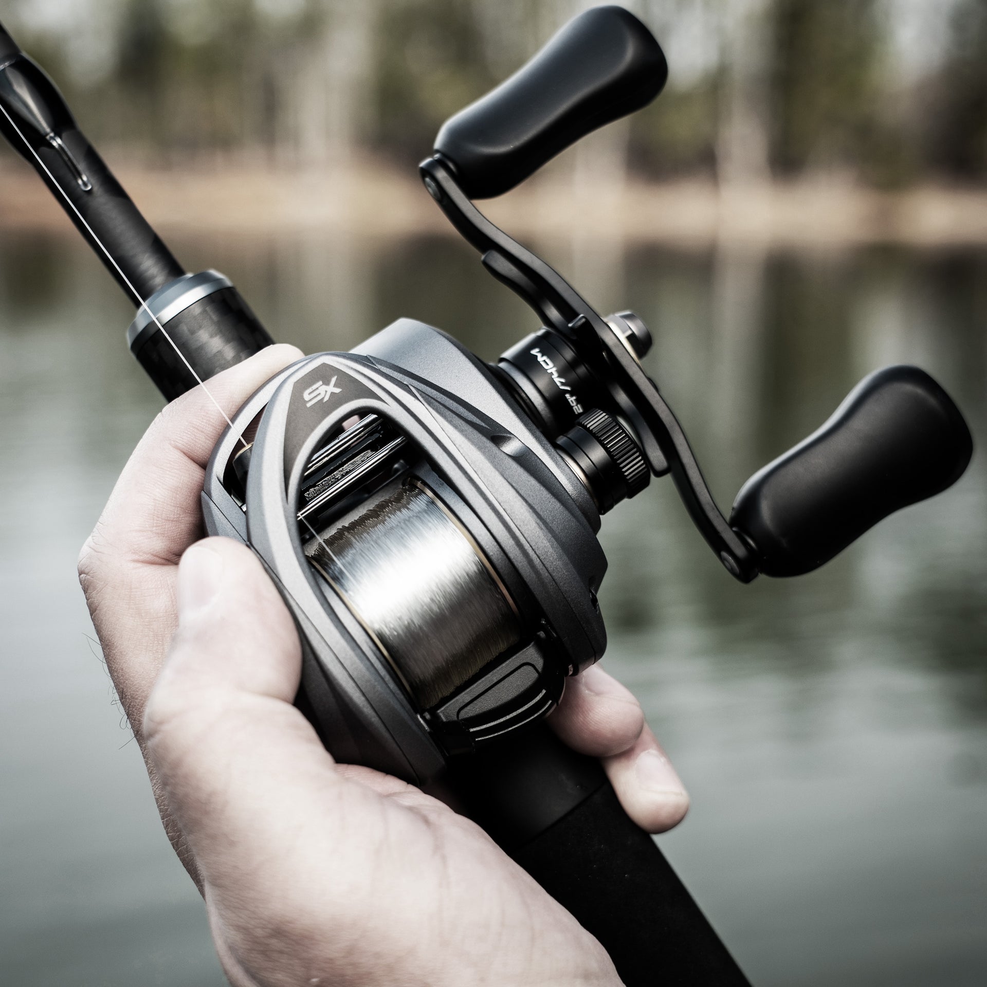 Fishing reel held in a hand with a blurred natural background