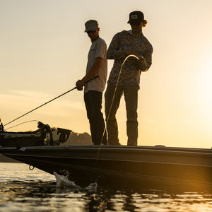 Two people on a boat at sunset, engaged in fishing.