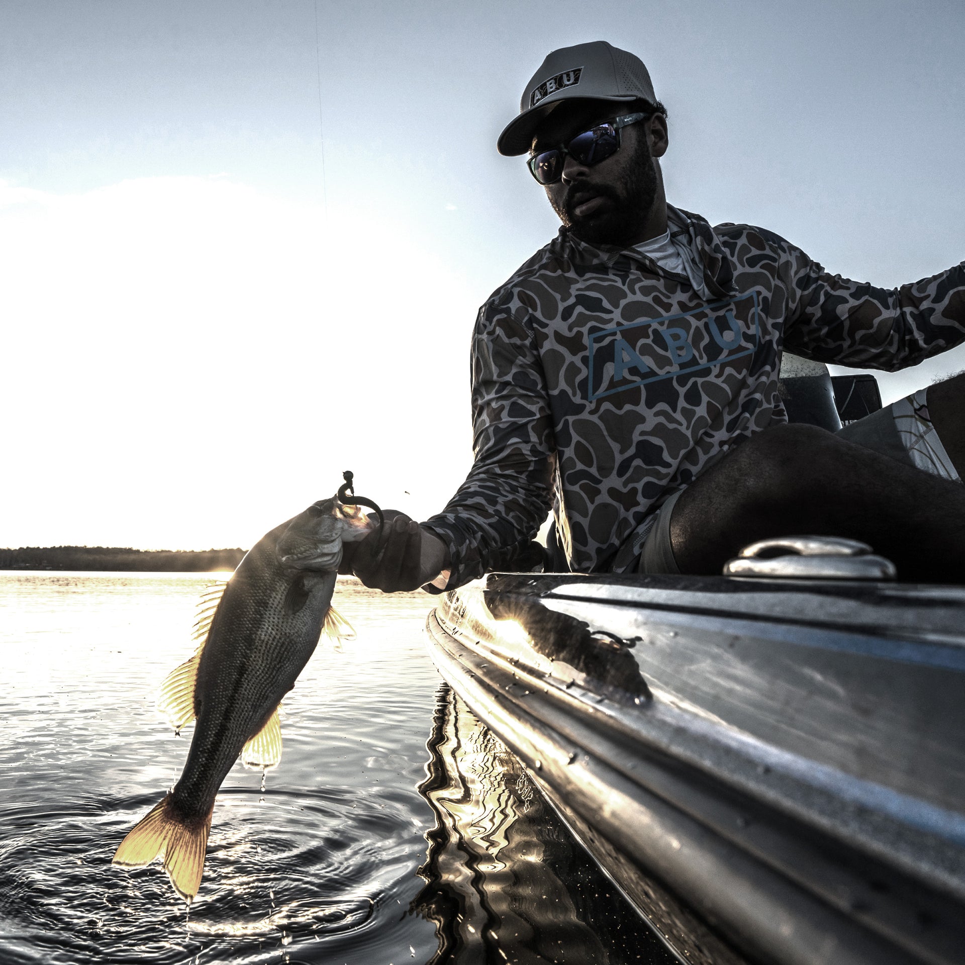 Man holding a fish on a boat with a lake background