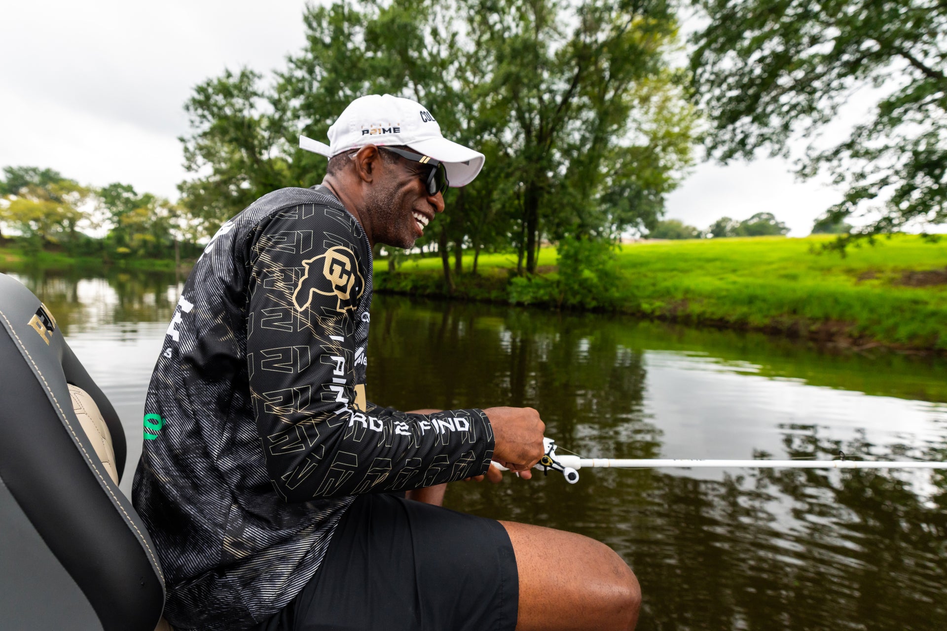 Man fishing on a boat by a river with trees and grass in the background