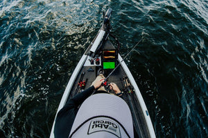 Overhead view of a person on a fishing boat holding a Abu Garcia Veritas Tournament Solid Tip rod, surrounded by dark blue water. The person wears a white and black shirt with the brand name 'Abu Garcia' visible on the hat. 